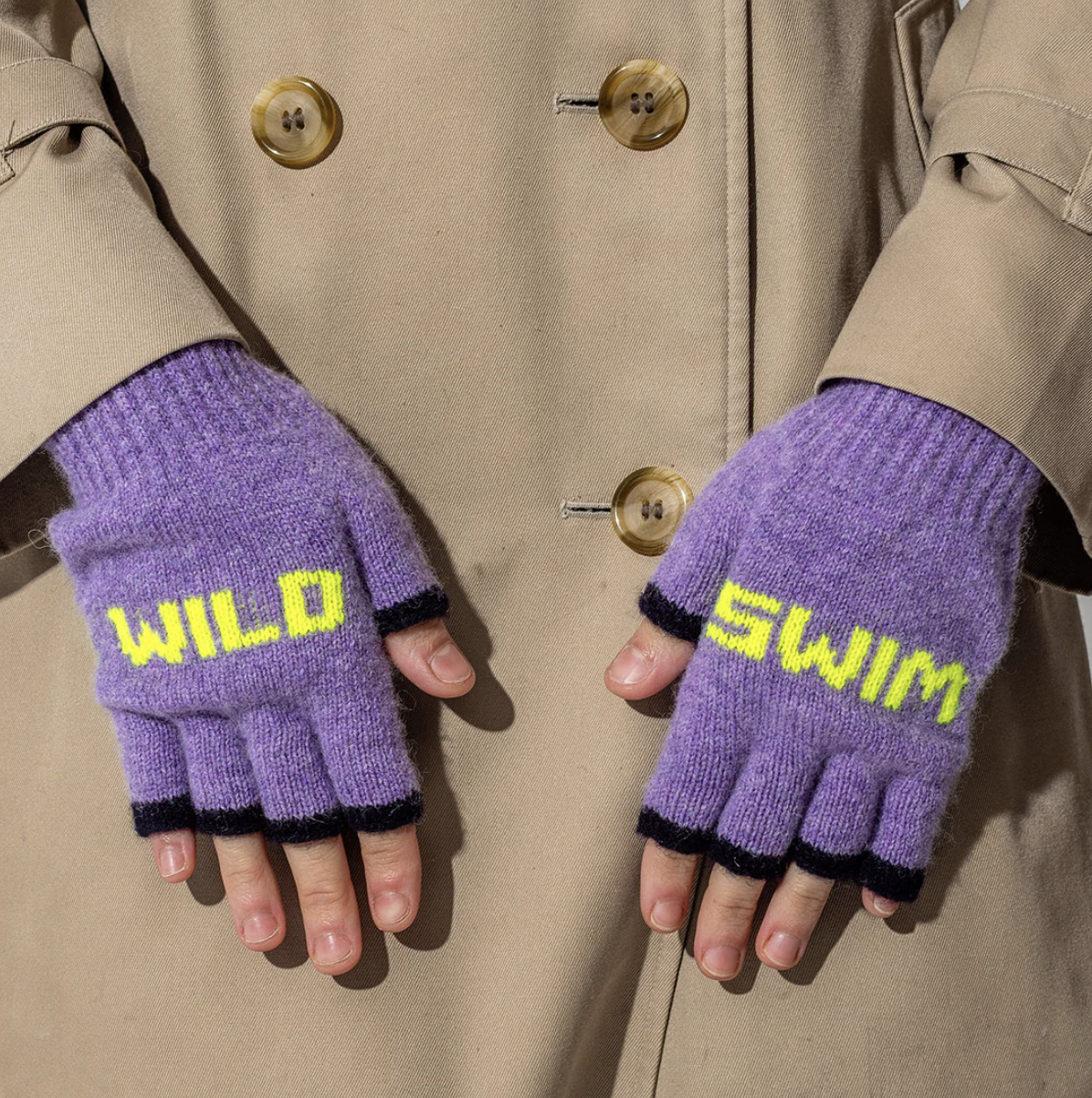Purple fingerless gloves with neon yellow 'WILD SWIM' text worn by a person in a beige trench coat. uk made 