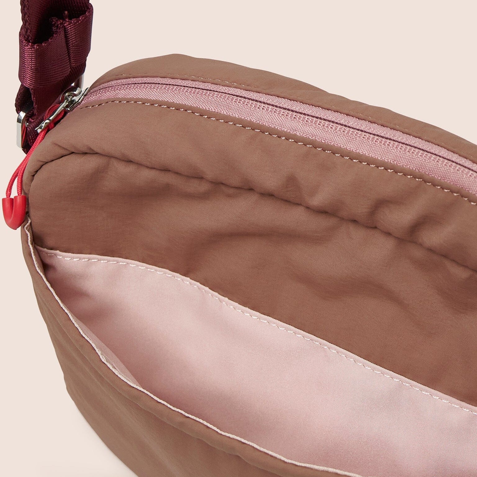 Close-up of a brown bag with a red zipper on a beige background