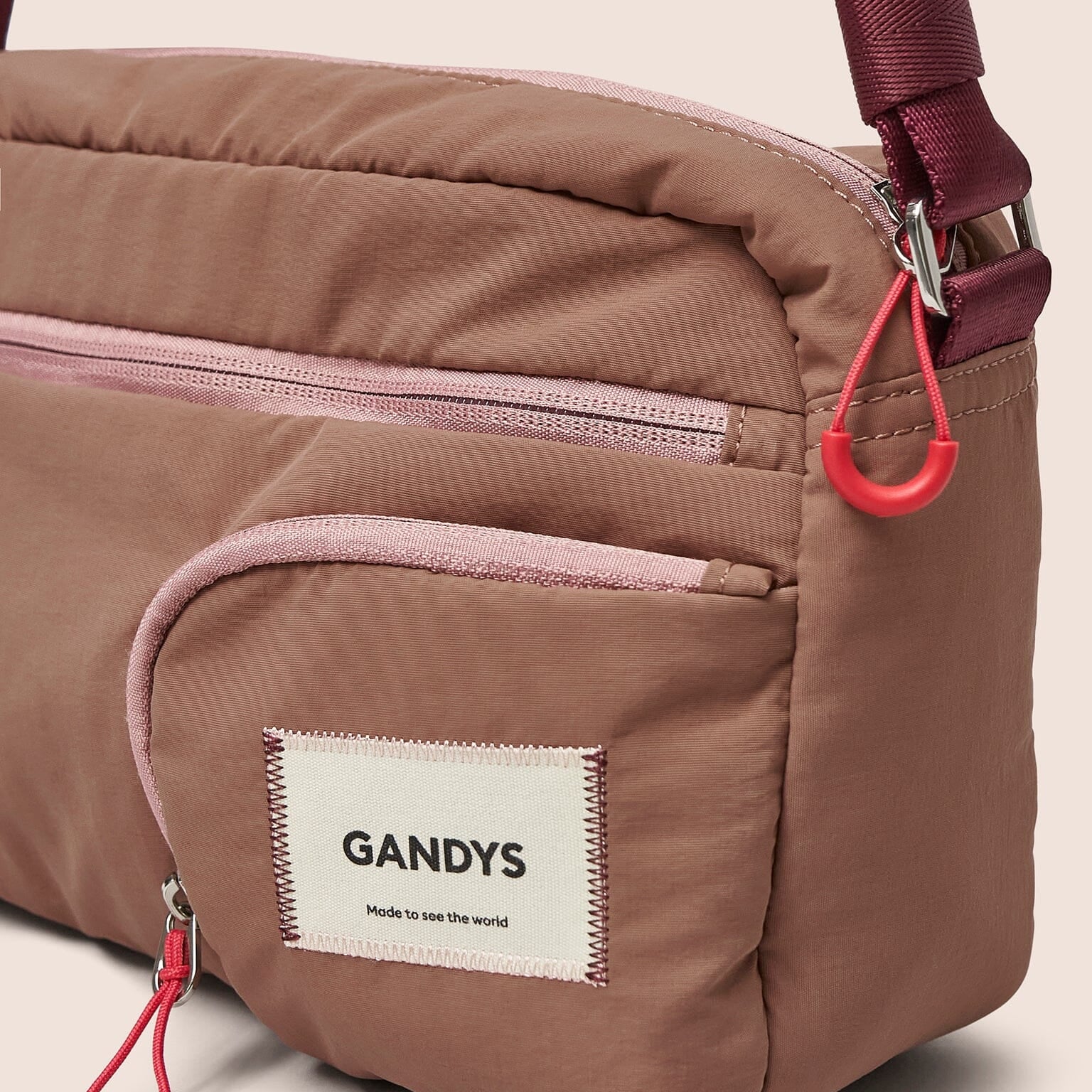 Brown shoulder bag with red zippers and a visible 'GANDYS' label on a beige background
