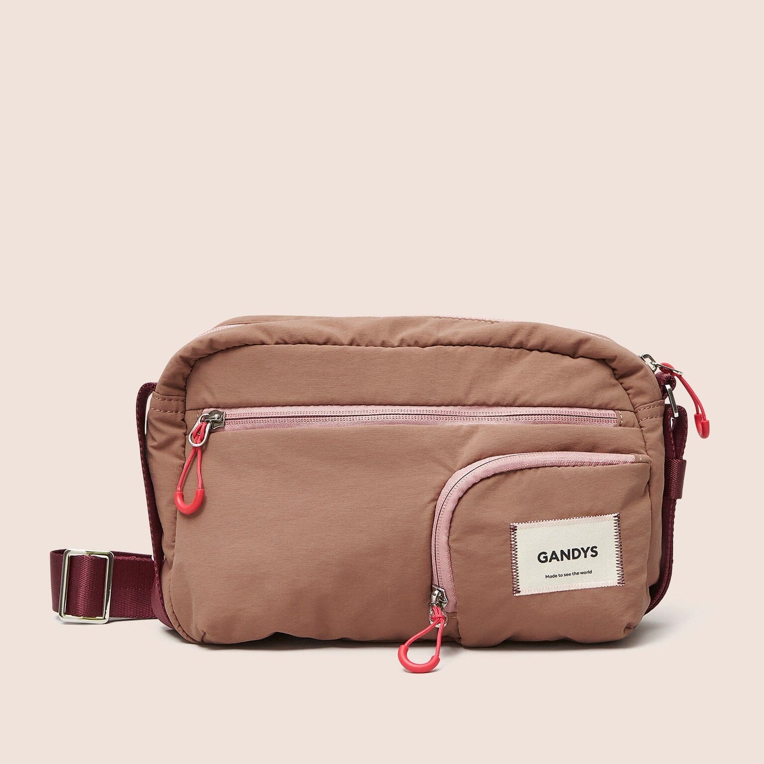 Gandys pink crossbody bag with pink accents on a beige background