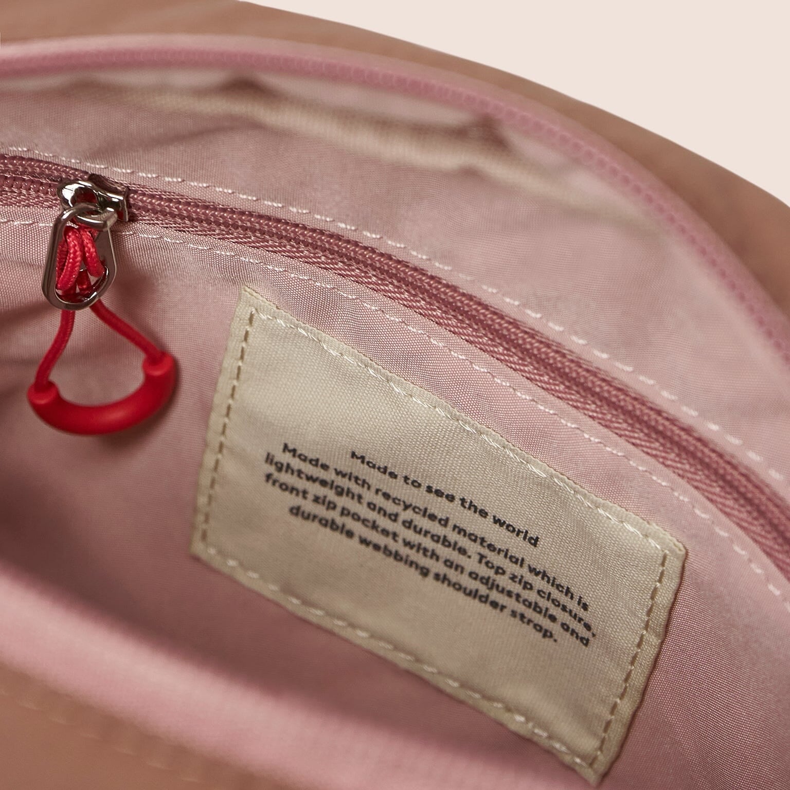 Close-up of a pink bag with a red zipper pull and a label on a beige background