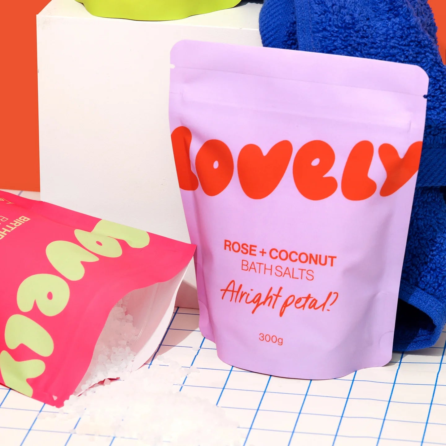 Purple packaging of 'Lovely' rose and coconut bath salts on a grid background