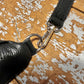 silver hardwear clip on black leather bag connecting strap to main bag, on a wooden surface 