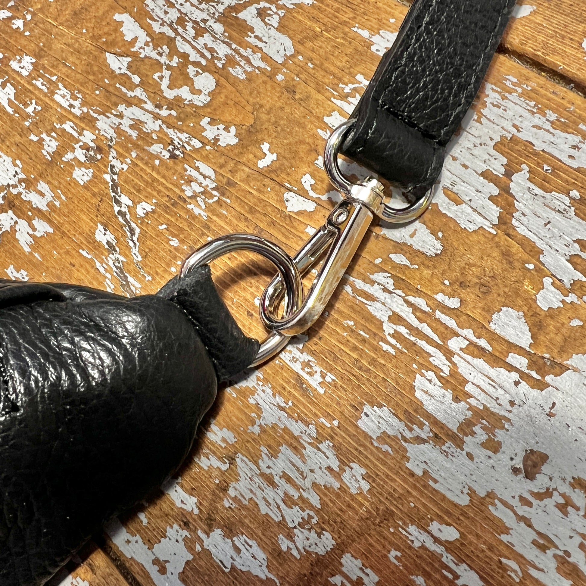 silver hardwear clip on black leather bag connecting strap to main bag, on a wooden surface 
