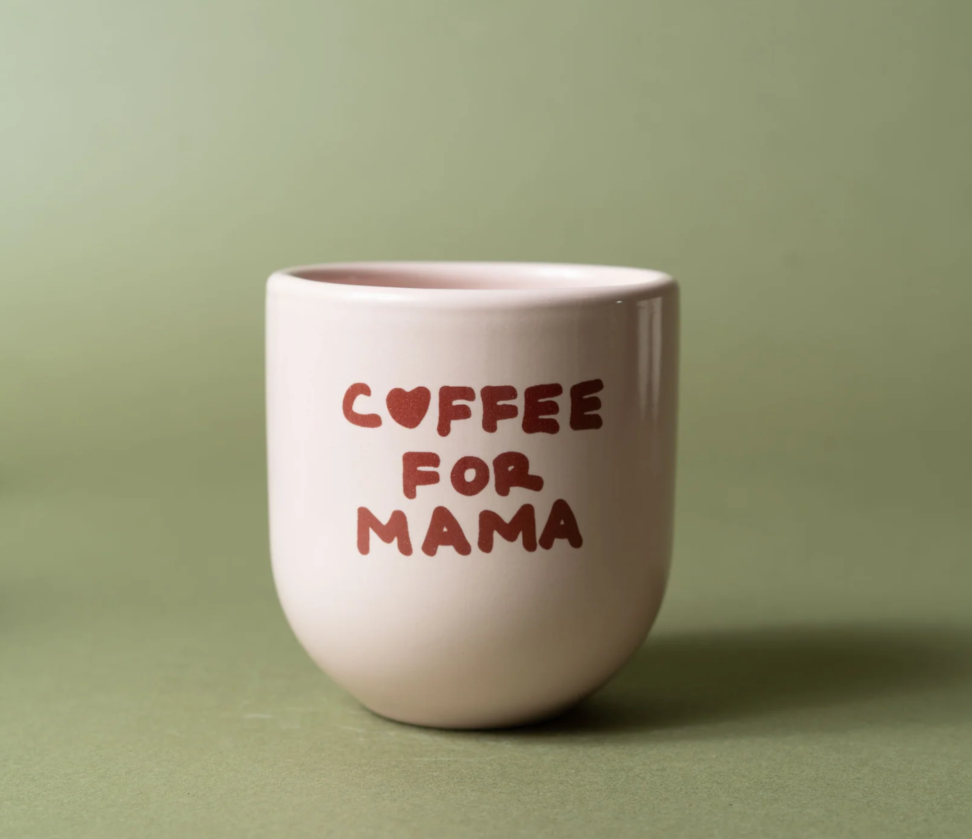 A small ceramic coffee mug with the words 'COFFEE FOR MAMA' printed in a dark red hand-drawn font, set against a solid sage green background.