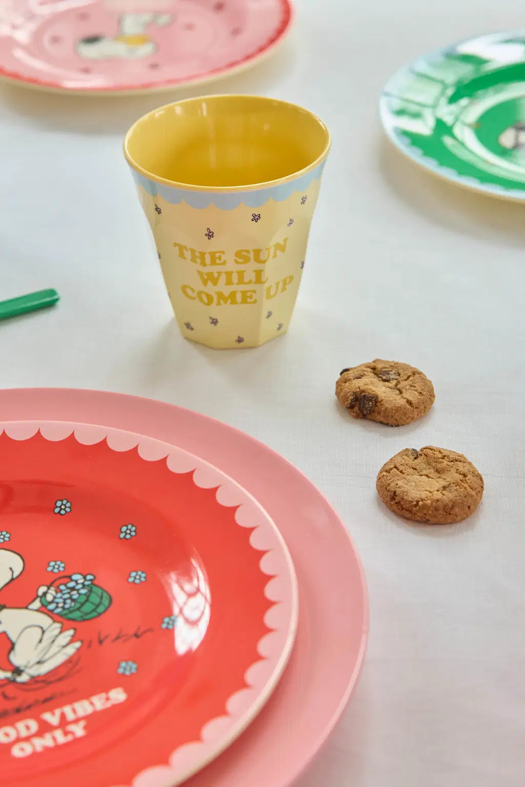 Colorful plates and a cup on a white surface with cookies.
