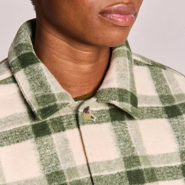 Close-up of a person wearing a green and cream plaid button-up shirt with a soft textured fabric.