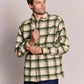 A man wearing a green and cream plaid button-up flannel shirt, paired with dark blue jeans, standing against a solid light gray studio background.