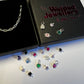 Black welded jewellery box open displaying a silver chain and colourful silver charms 