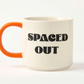 white mug with orange handle and black 'SPACED OUT' text on a white background