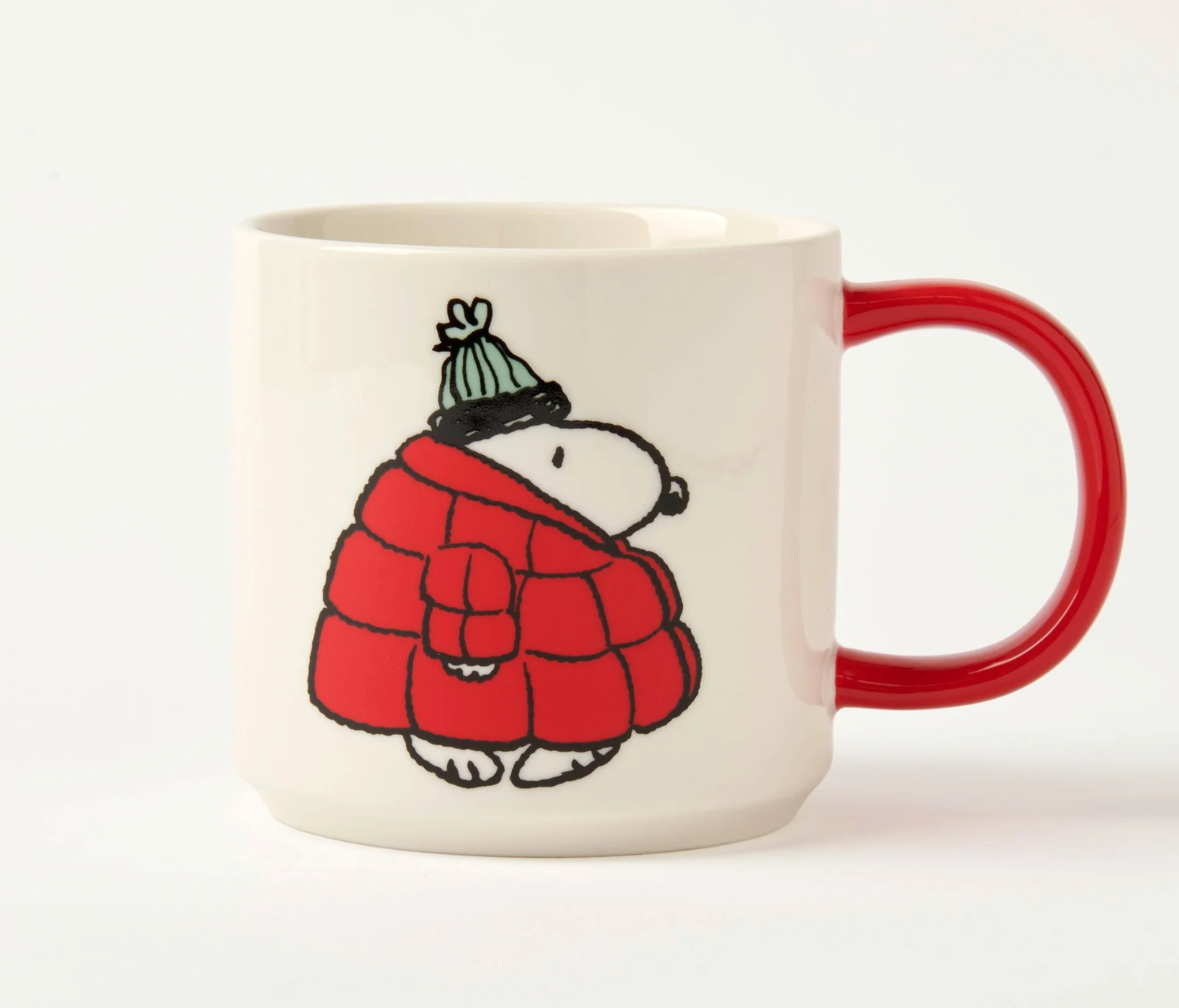 white mug with red handle. cartoon snoopy dog wearing a big red puffer coat and green bobble hat on a white background